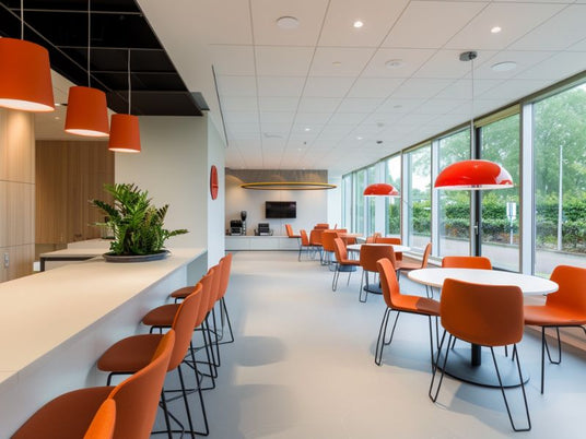 Witte plafondplaten boven zithoek met oranje designstoelen