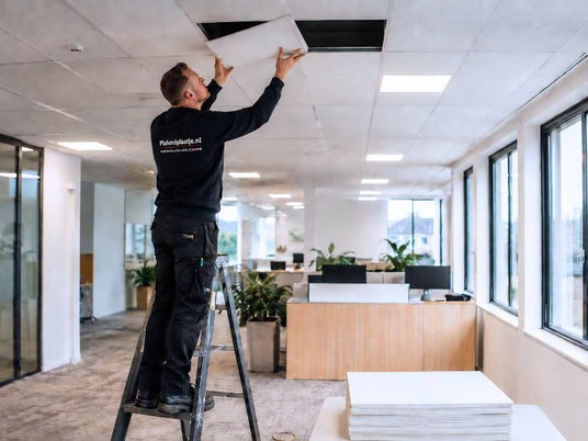 Een monteur van Plafondplaatje.nl plaatst plafondplaten in een strak systeemplafond binnen een moderne zakelijke kantoorruimte. Plafondplaatje.nl levert plafondplaten snel uit voorraad en kan ook montage op locatie verzorgen.